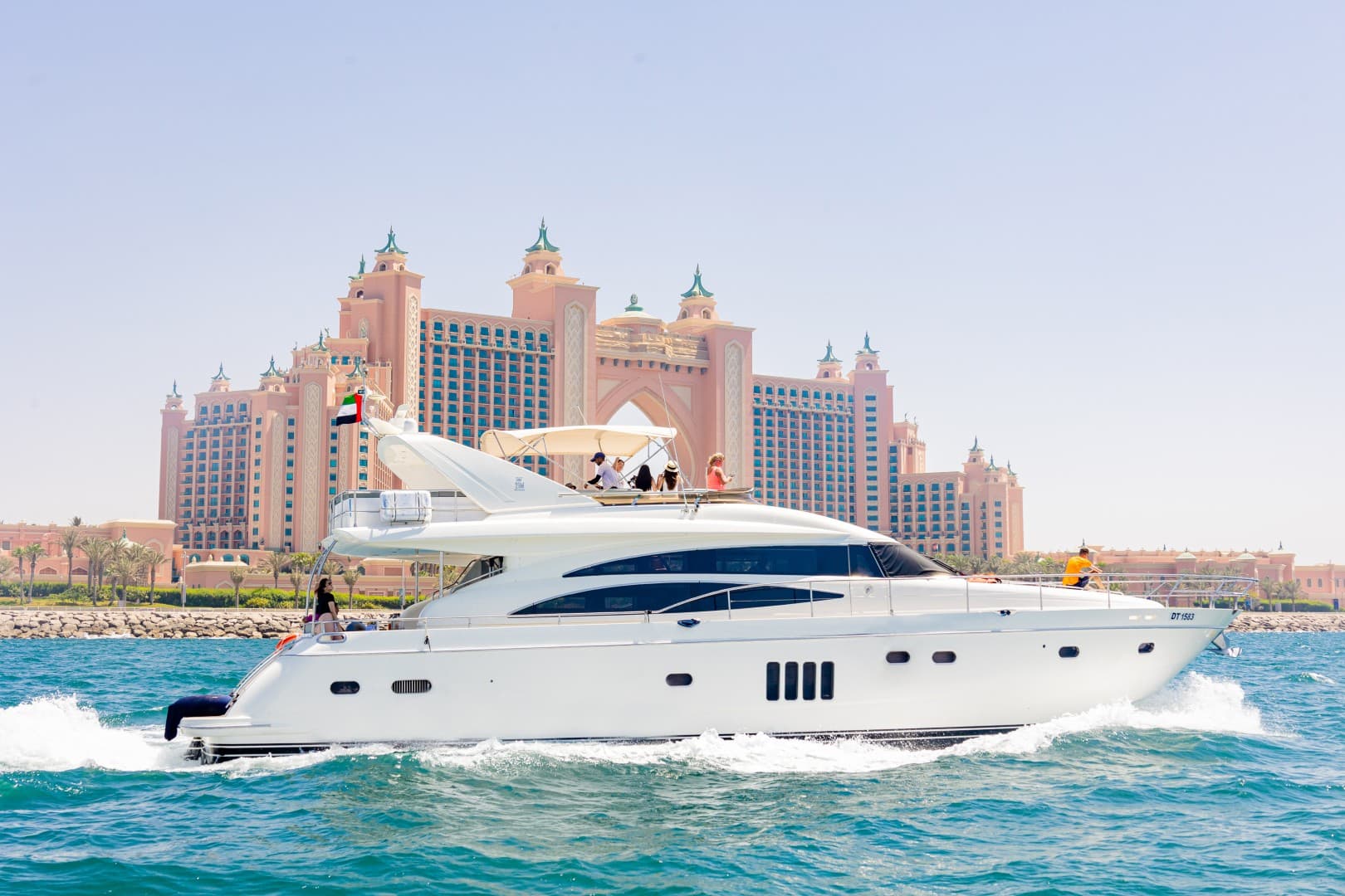 A white boat floating on water near the Burj Coastline, with the Atlantis Hotel in the background.