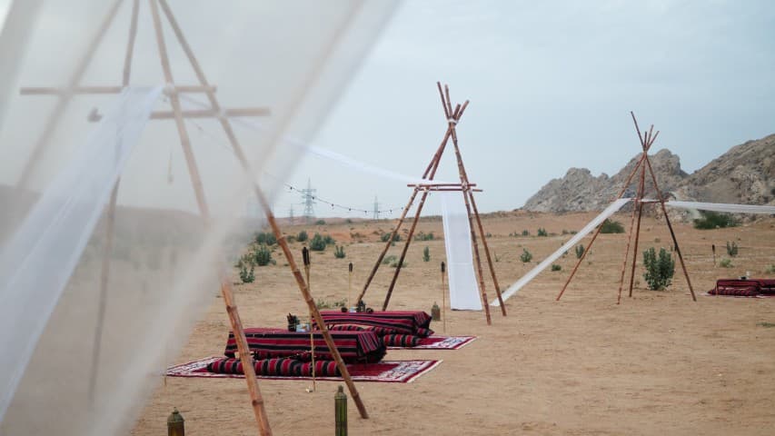 A tent with a canopy and a bed set up in the desert, with a buggy nearby for camp dinner during the daytime.