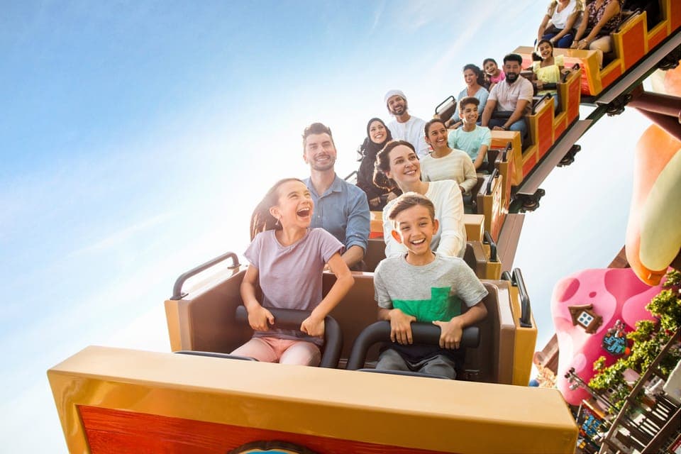 A group of people, including children and adults, enjoy a thrilling roller coaster ride under a clear blue sky