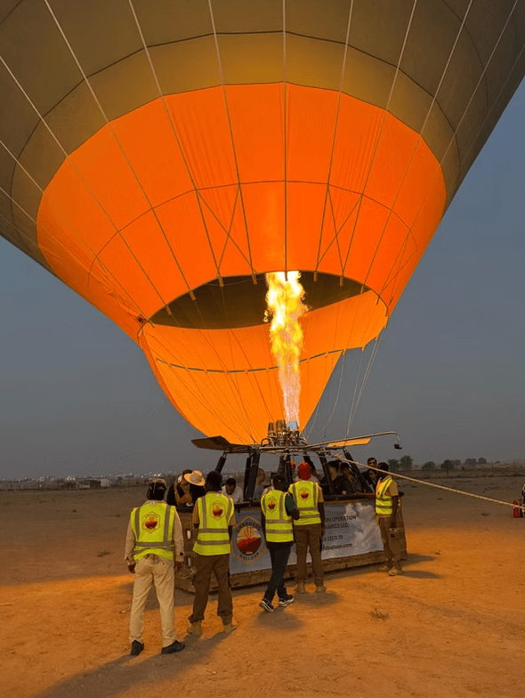 People in yellow vests prepare a hot air balloon for launch at dusk.