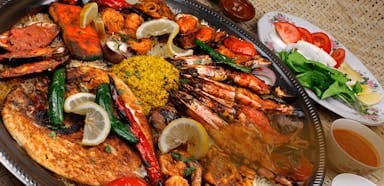 A large silver platter brimming with grilled seafood, including shrimp, fish, and crab, garnished with lemon wedges.