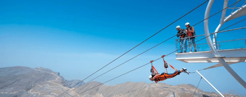 A man soaring on a zip line over the mountains at Jebel Jais, showcasing the stunning landscape below.