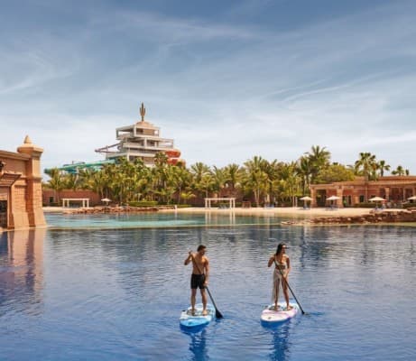 Two people on paddle boards in front of Dolphin Paddle resort, enjoying a sunny day on the lagoon.