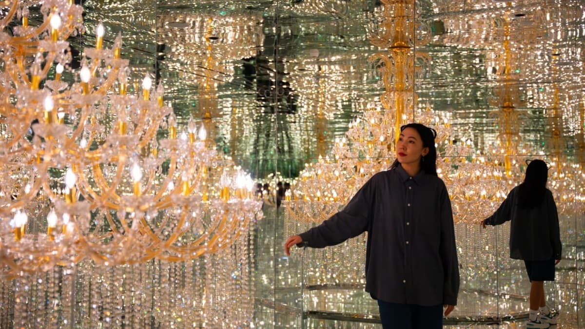 A woman stands in front of a mirror, surrounded by elegant chandeliers at House of Hype in Dubai.