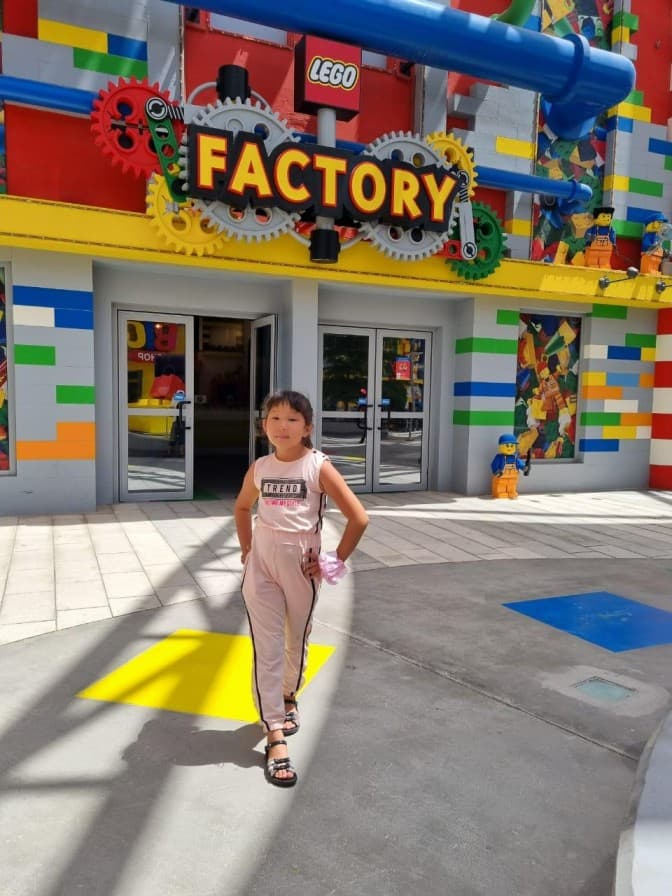 Girl in a pink outfit stands confidently outside the colorful LEGO Factory,