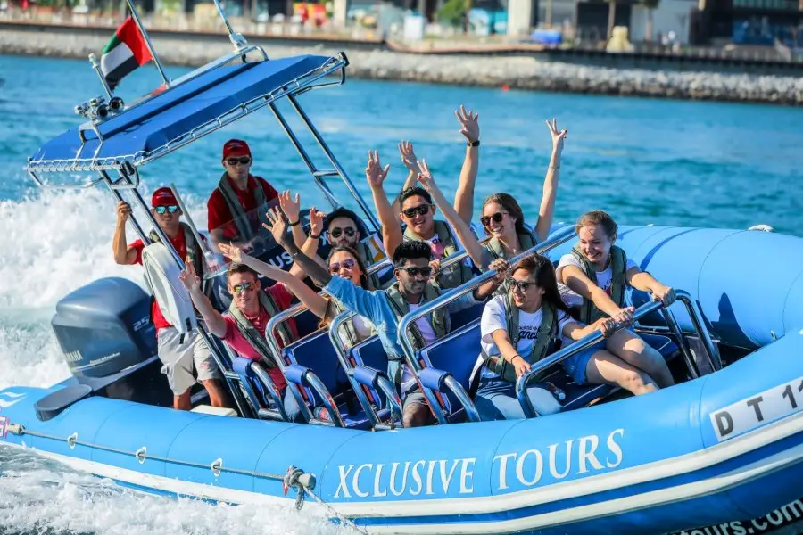 A group of excited people on a blue speedboat labeled "Xclusive Tours," smiling and raising their arms