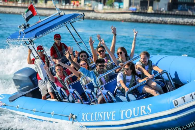 A group of excited people on a blue speedboat labeled "Xclusive Tours," smiling and raising their arms