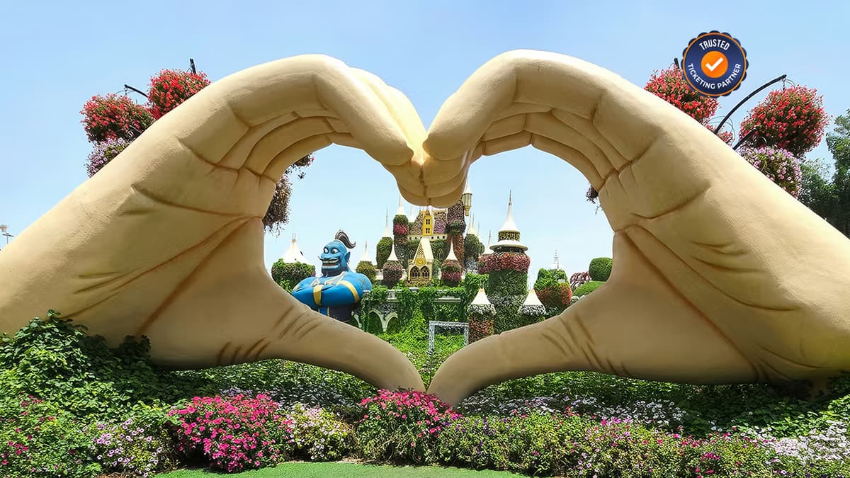 Visitors making a heart shape with their hands in front of the floral love symbol at Dubai Miracle Garden.