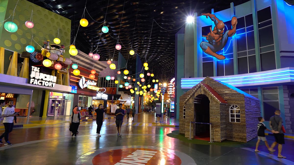 A busy mall scene with people walking and a large Spider-Man figure prominently displayed.