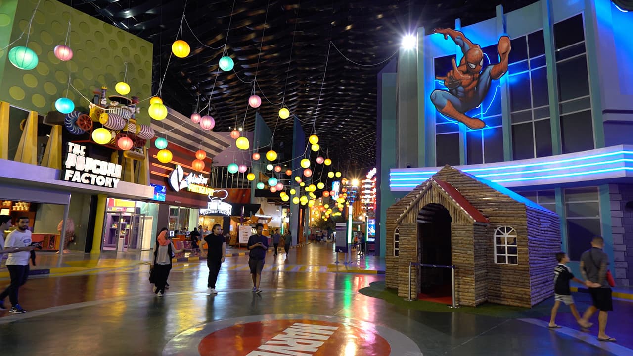A busy mall scene with people walking and a large Spider-Man figure prominently displayed.