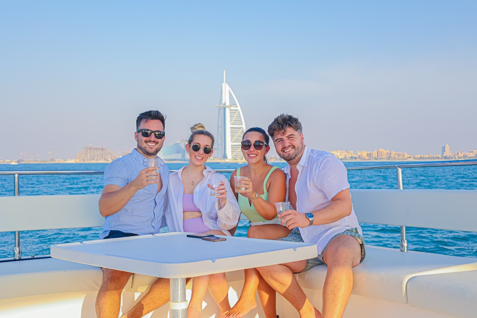 Four people enjoying a glass of wine while sitting on a boat during the Burj Coastline Tour group photo.