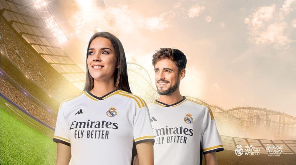 Male and female smile confidently wearing white Real Madrid jerseys with a bright stadium backdrop