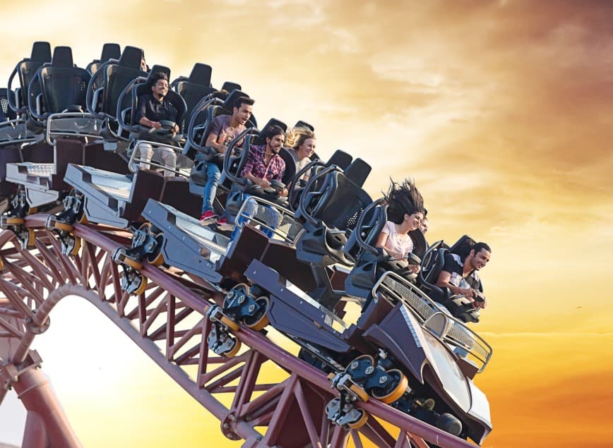 A group of people ride a roller coaster against a vibrant sunset sky