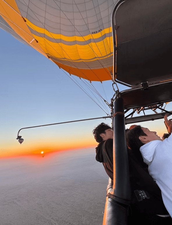 A hot air balloon at sunrise, with two people in the basket looking out. 