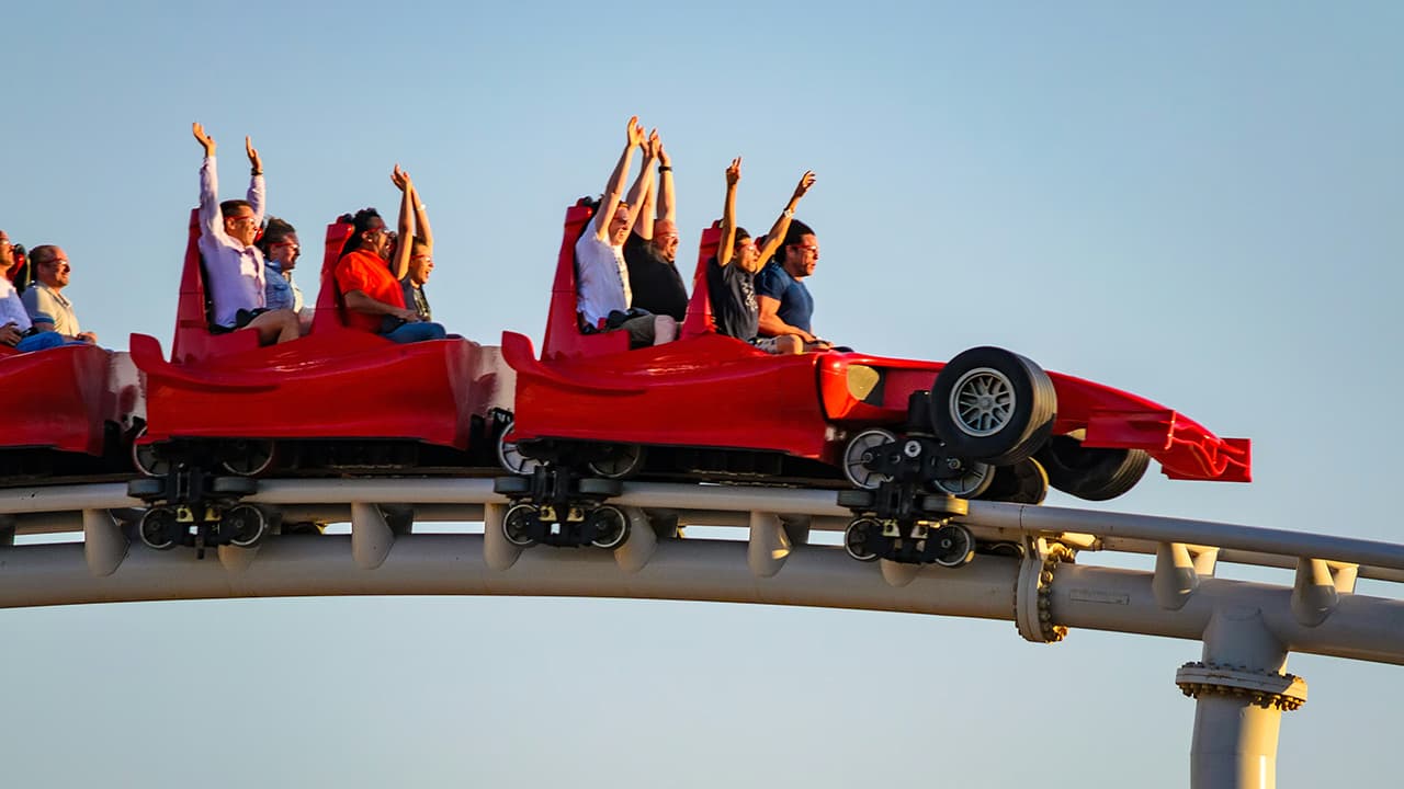 A group of excited people enjoying a thrilling ride on a roller coaster in Ferrari World Abu Dhabi, with their hands raised in the air.