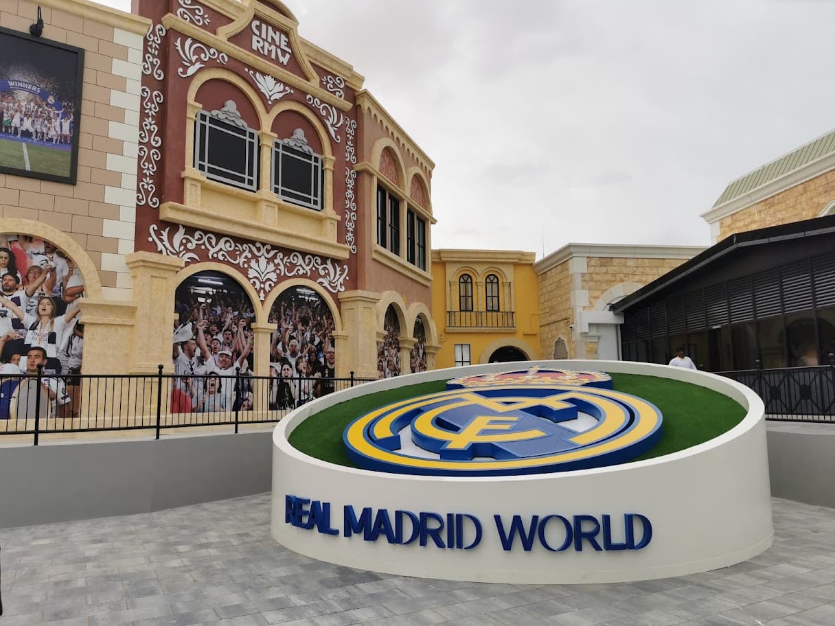 The image shows the entrance to "Real Madrid World" featuring a large round emblem with the club's logo