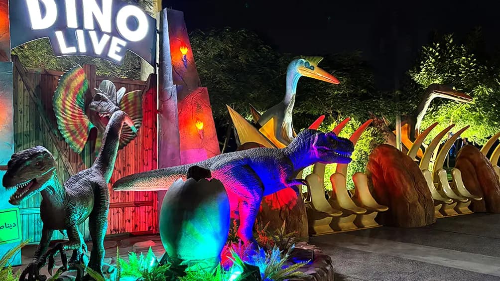 Life-size dinosaur models displayed in a themed outdoor Dinosaur Park with visitors exploring the attraction.