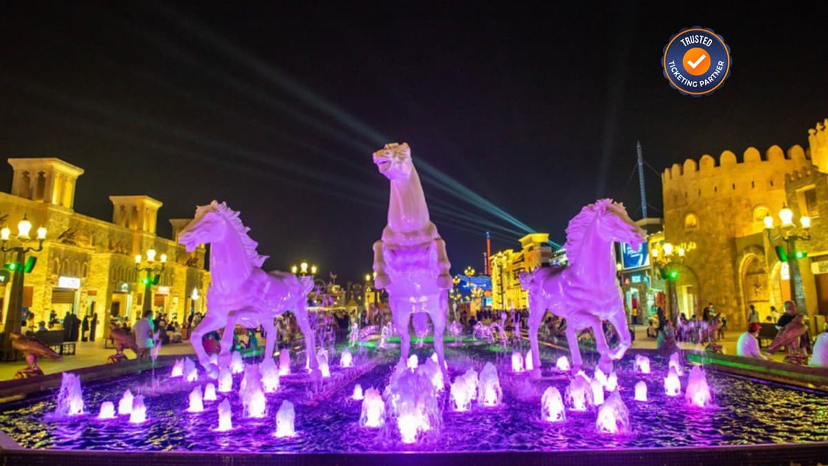 Illuminated horse statues rise from a vibrant purple fountain against a night sky.