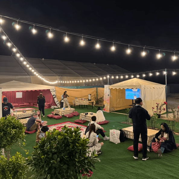 Outdoor night scene with string lights illuminating a cozy tent area. 