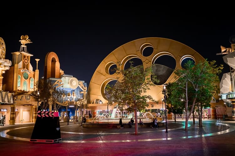 Nighttime amusement park plaza with ornate, whimsical architecture, and a relaxed atmosphere.