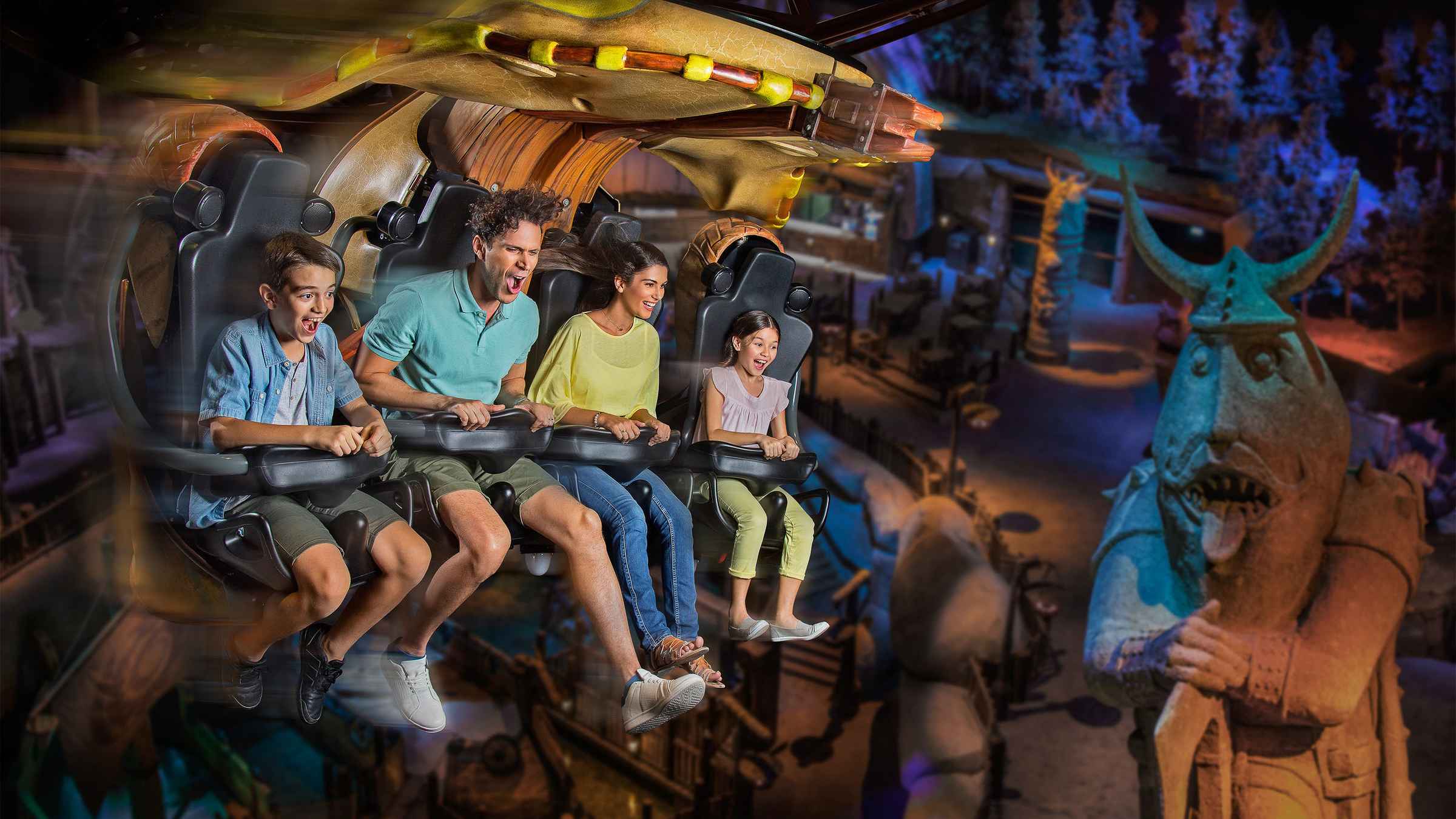 A family of four enjoys a thrilling amusement park ride. A large whimsical statue in the background adds a playful touch.