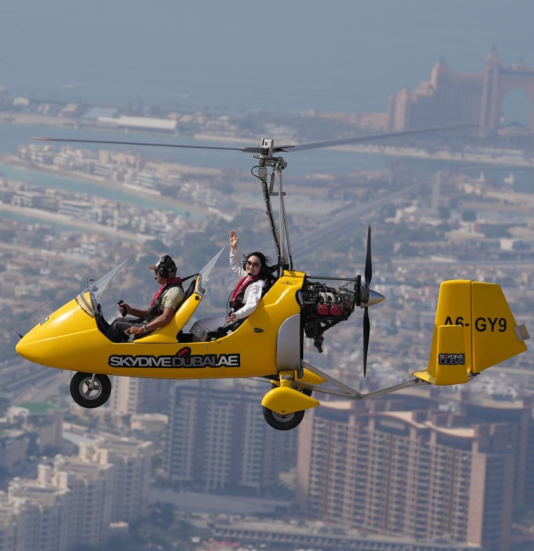 A small yellow gyrocopter flying over a cityscape, labeled 'Gyrocopter Flight-Atlantis'.