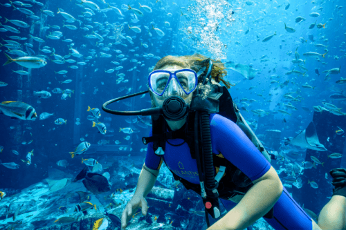 A woman scuba diver surrounded by colorful fish in the water, showcasing a vibrant underwater scene.