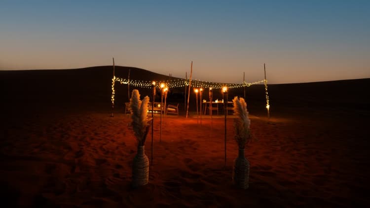 A serene desert evening scene with a cozy dining setup under string lights. 