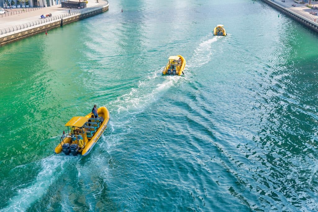 Three yellow boats from the Abu Dhabi fleet tour glide down a river under clear skies.