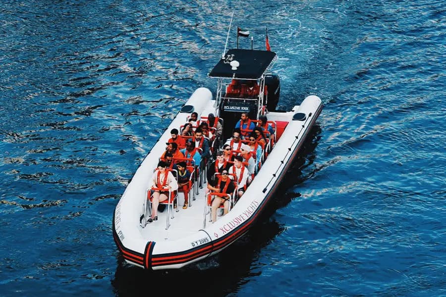 A white and red inflatable speedboat carries a group of people in life jackets across a deep blue ocean.
