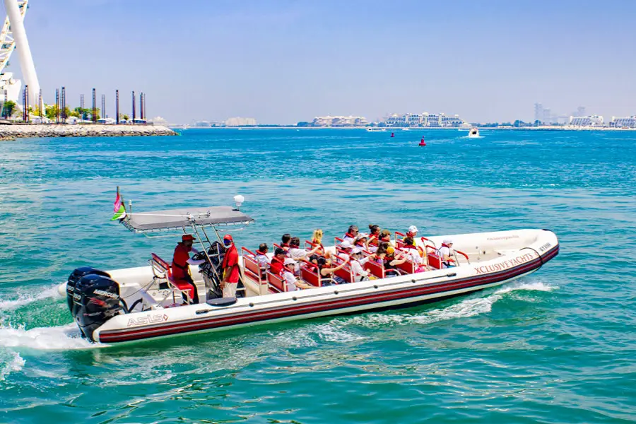 A motorboat filled with tourists in life jackets speeds across a bright blue sea under a clear sky. 