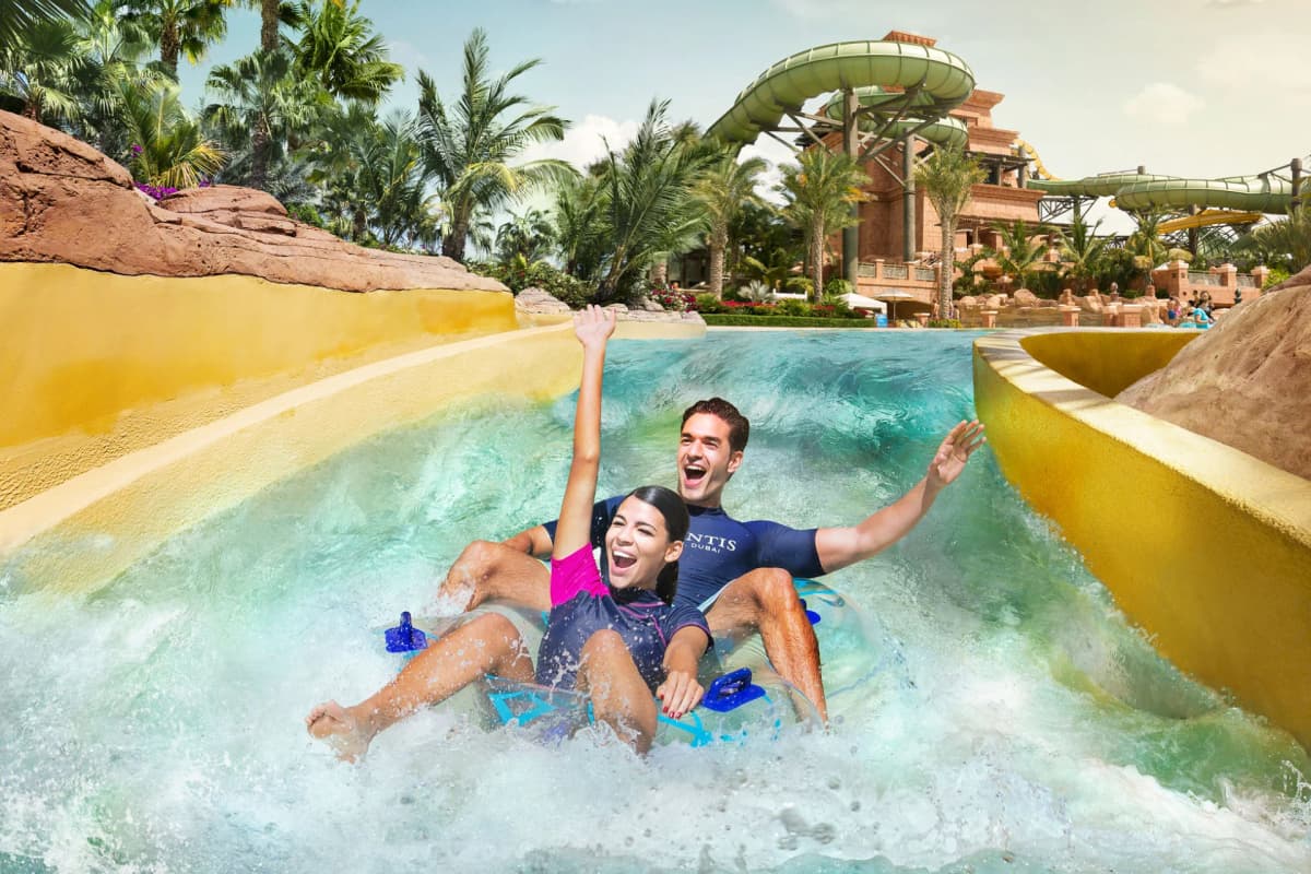 Two people joyfully riding a water slide at Atlantis Aquaventure water park, surrounded by splashes and excitement.