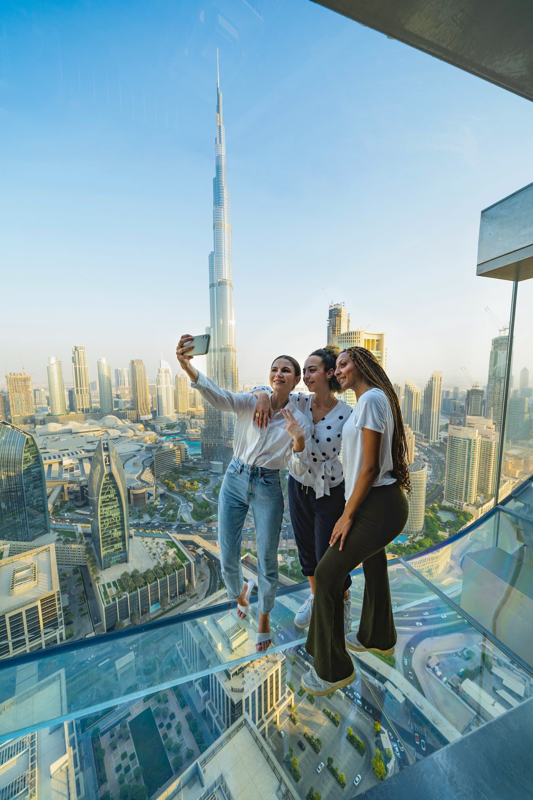 Friends capturing a fun photo moment together at Sky Views Dubai with the city skyline behind them