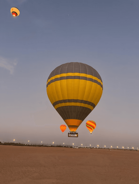 Hot air balloons soar against a twilight sky, with the largest being gray and yellow. 