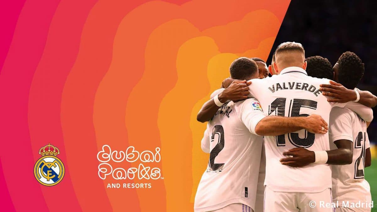 Soccer players in white jerseys embrace in celebration. Real Madrid and Dubai Parks logos are visible.