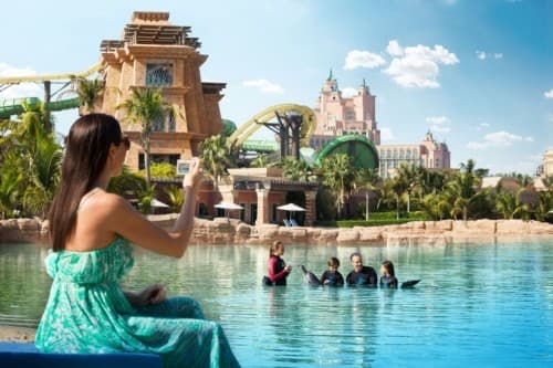 A woman captures a photo at Atlantis Aquaventure water park, surrounded by slides and attractions.