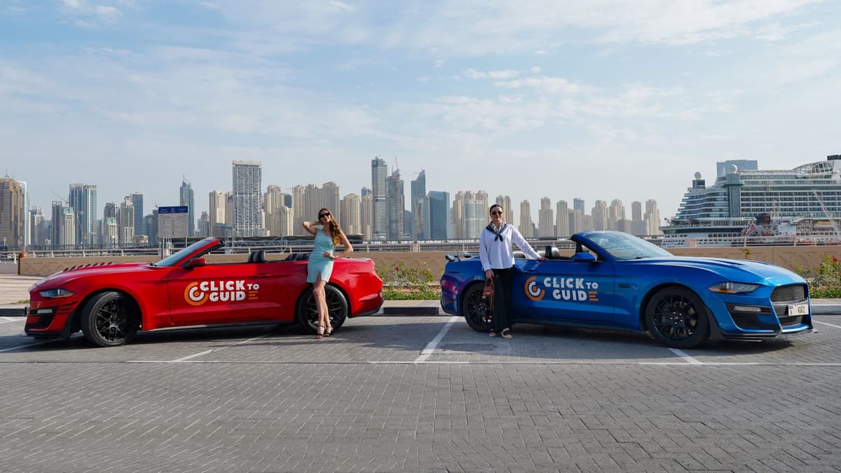 Two convertible cars, one red and one blue, parked side by side with the backdrop of a city skyline. 