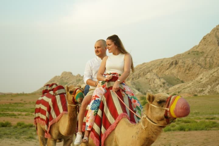 Camel riding in the desert during the Mleiha Buggy experience, showcasing the vast sandy landscape and clear blue sky.