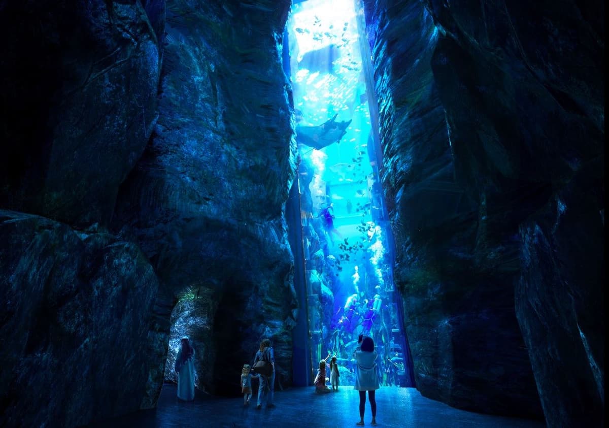 People walking through a blue-lit tunnel in the SeaWorld Abu Dhabi Dungeon, creating an immersive atmosphere.