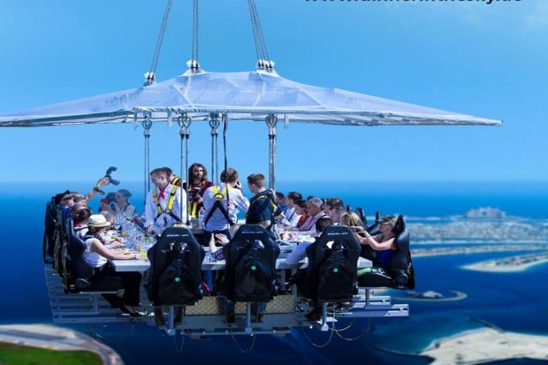 A group of people dining at a table suspended in the sky, enjoying a unique aerial dining experience.