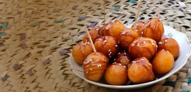 Plate of round, golden fried sweets topped with caramel and sesame seeds, pierced with toothpicks, on a woven mat, creating a cozy, inviting feel.
