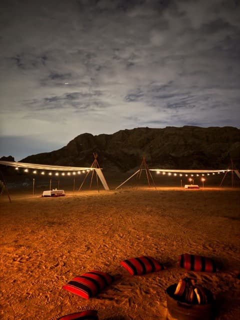 A tent in the desert with a fire pit and chairs, set up for a camp dinner.