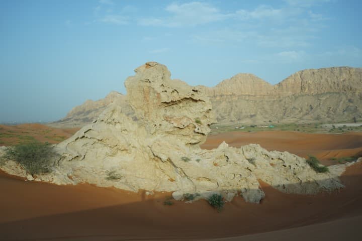 A rock formation in the desert with mountains in the background, showcasing the Mleiha Buggy archaeological site.