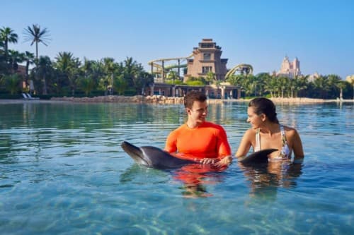 Two people interact with dolphins in the water at Aquaventure Waterpark in Dubai.