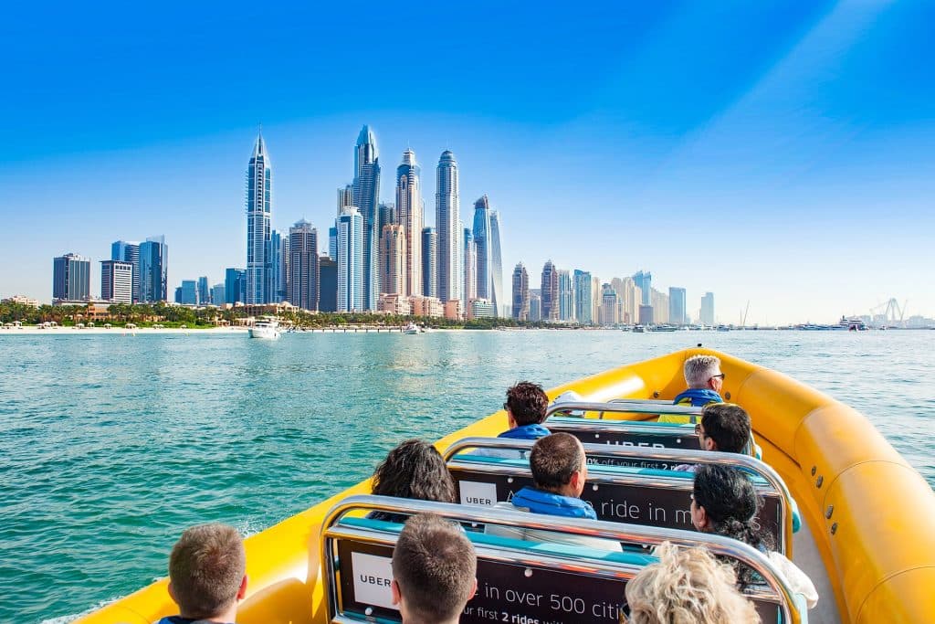A group on a yellow speedboat views a stunning modern skyline across a calm sea