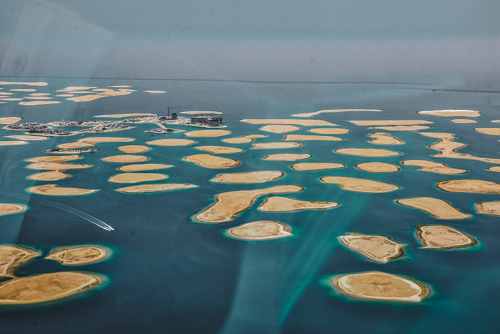 Aerial view of an archipelago showing numerous small, sandy islands surrounded by turquoise water, with a distant boat. 