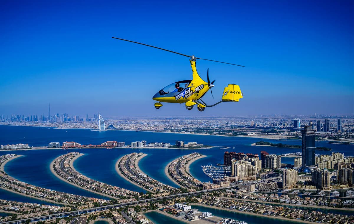 A gyrocopter flying over the city of Dubai, showcasing the skyline and iconic landmarks below.