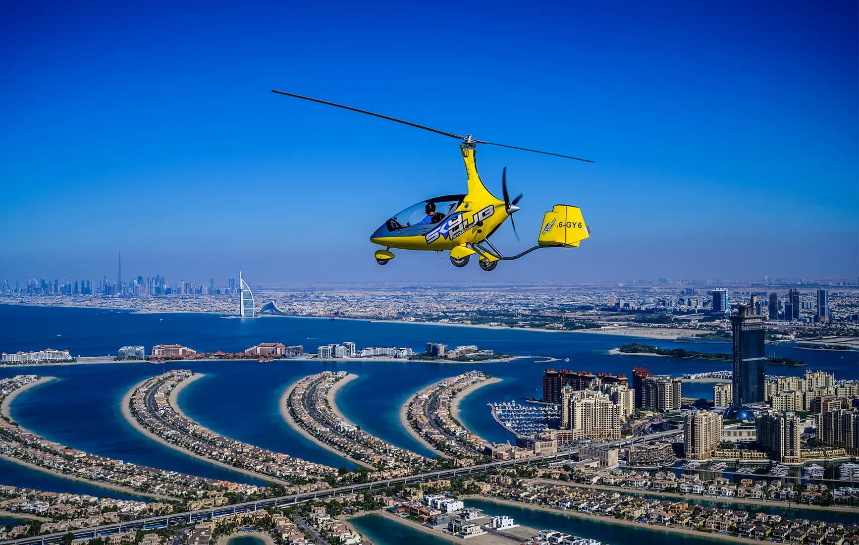 A gyrocopter flying over the city of Dubai, showcasing the skyline and iconic landmarks below.