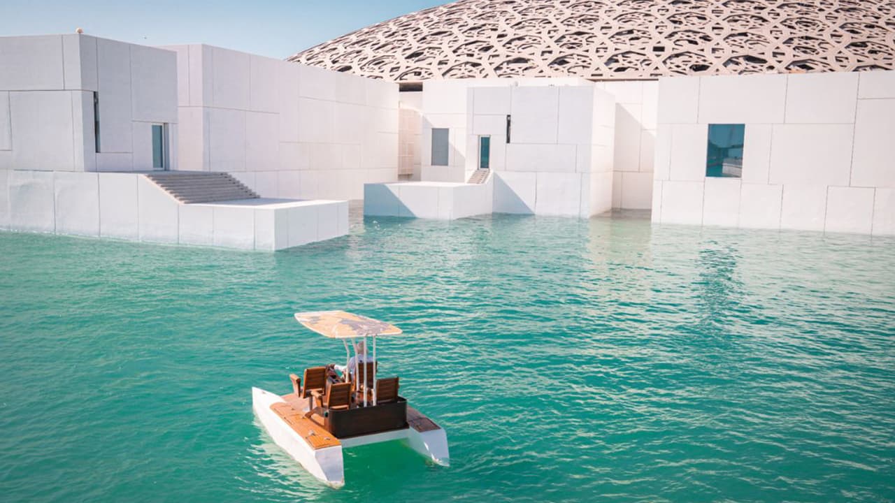 A boat floats in the water near Louvre Abu Dhabi, creating a serene waterfront scene.