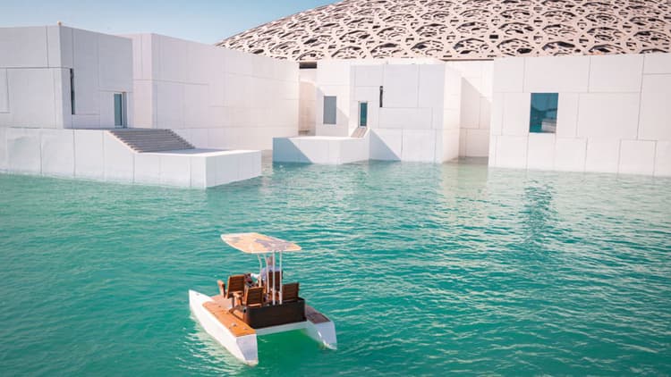 A boat floats in the water near Louvre Abu Dhabi, creating a serene waterfront scene.